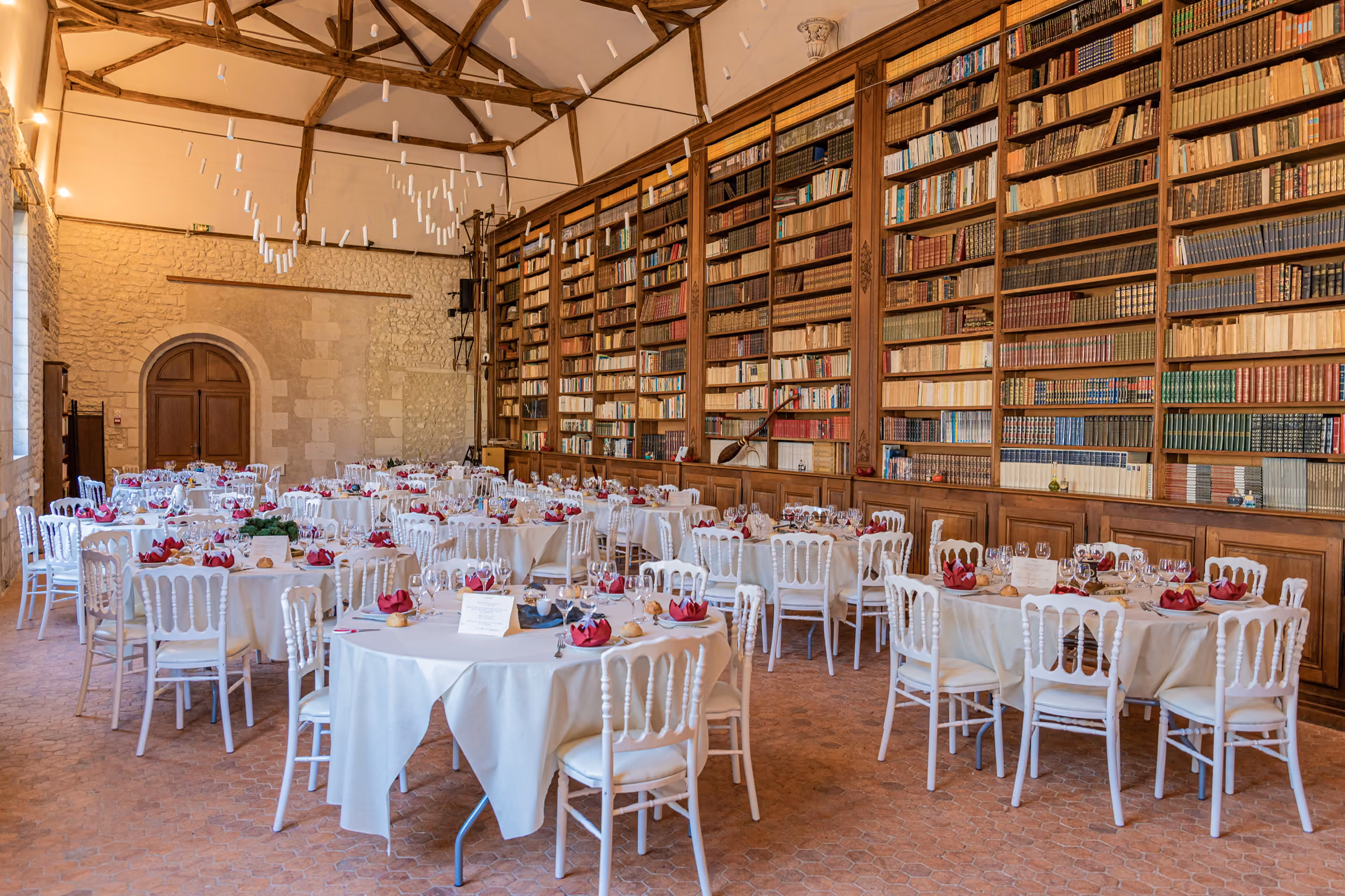 Bibliothèque du château dressée en lumière du jour avec tables rondes et serviettes bordeaux
