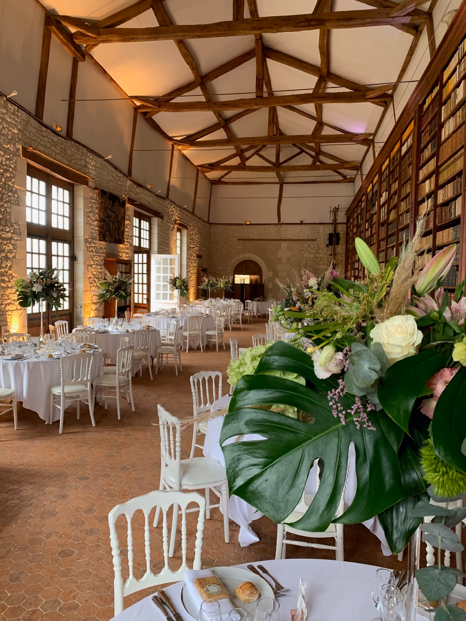 Grande salle de réception à charpente apparente dressée pour un banquet devant la bibliothèque
