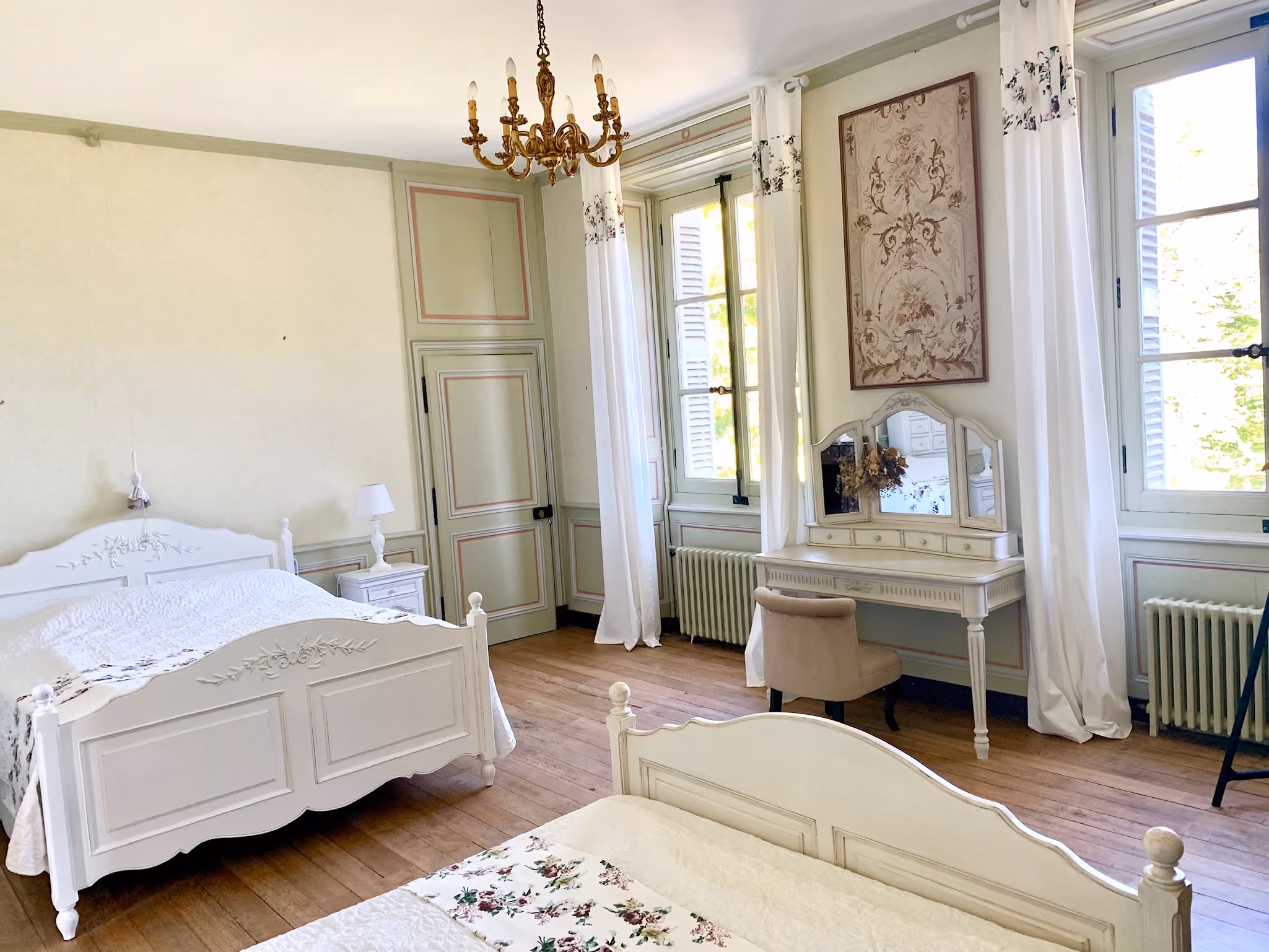 Chambre d'hôtes aux boiseries vert amande avec lits en bois peint et coiffeuse ancienne
