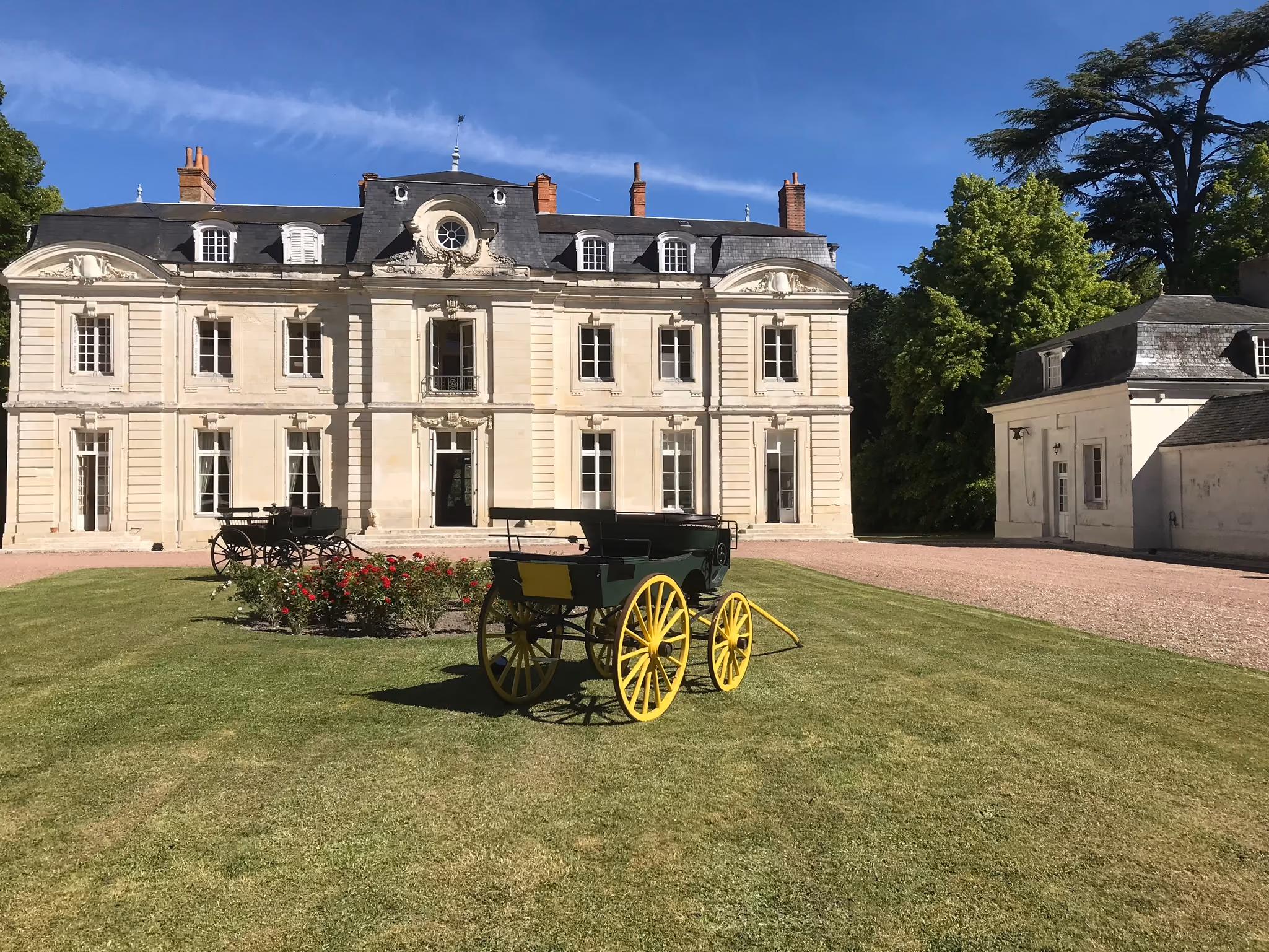 La façade XVIIIe du château sous un ciel bleu, bordée d’un cèdre et de pelouses
