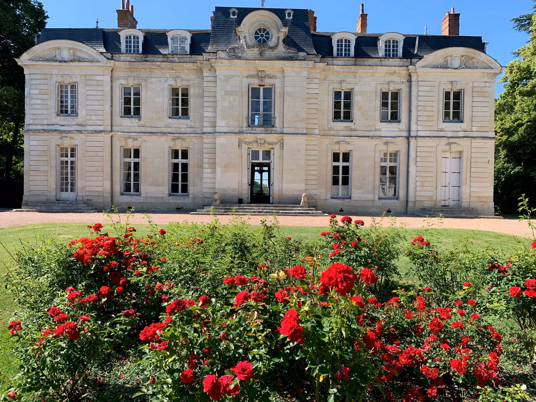 Façade XVIIIe du château vue de face derrière un massif de rosiers rouges en pleine floraison