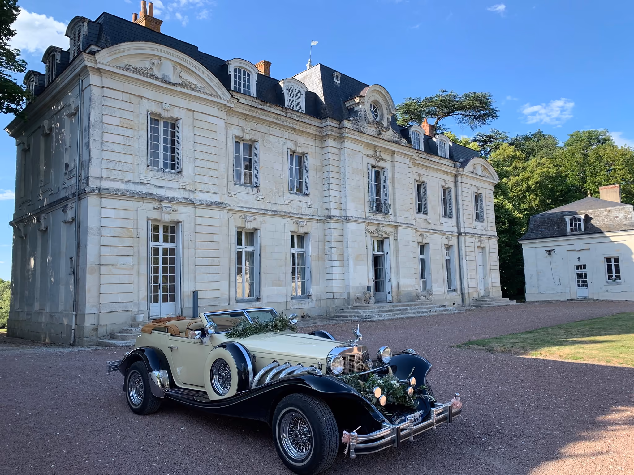 Voiture de collection fleurie devant la façade en tuffeau du château un jour de mariage