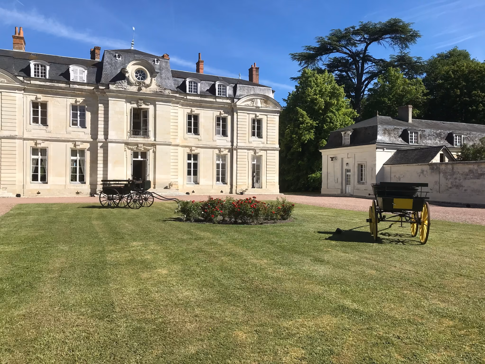 Cour d'honneur du château avec deux calèches anciennes et un massif de rosiers rouges
