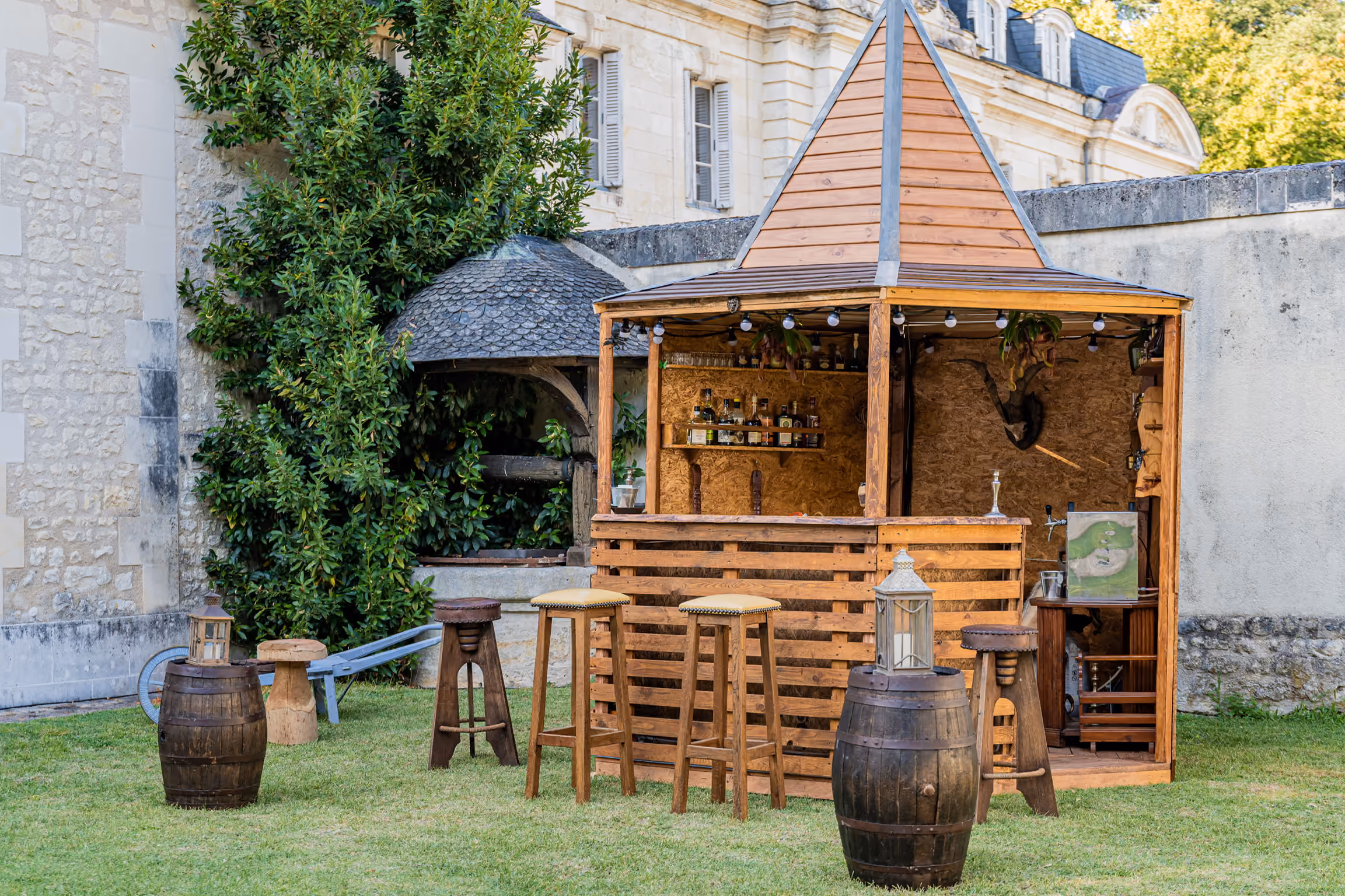 Bar en bois installé sur la pelouse du domaine avec tabourets et tonneaux pour un cocktail