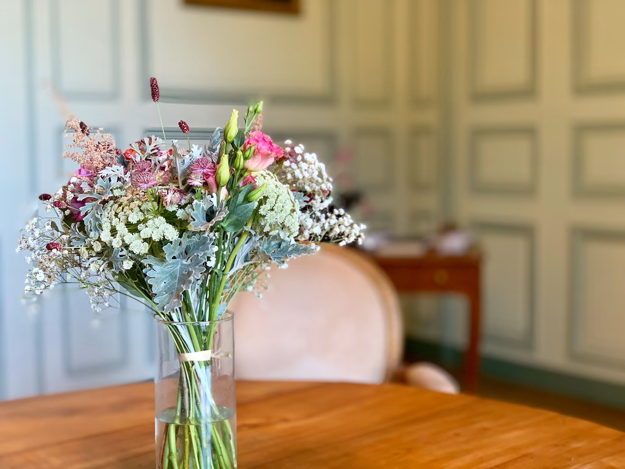 Bouquet champêtre rose et blanc dans un vase de verre posé sur une table de salon