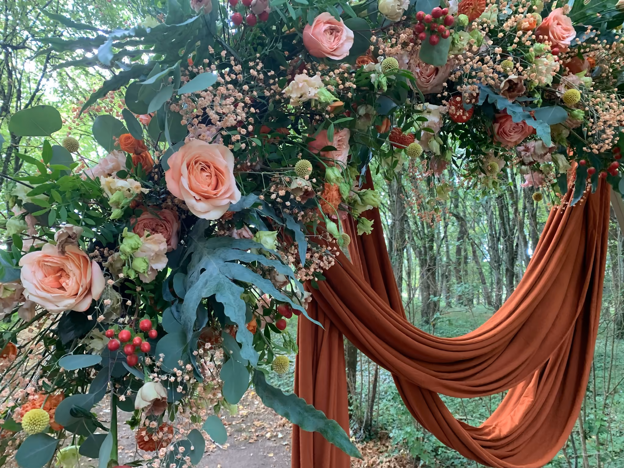 Arche florale de cérémonie en roses et voilage terracotta installée en lisière de sous-bois