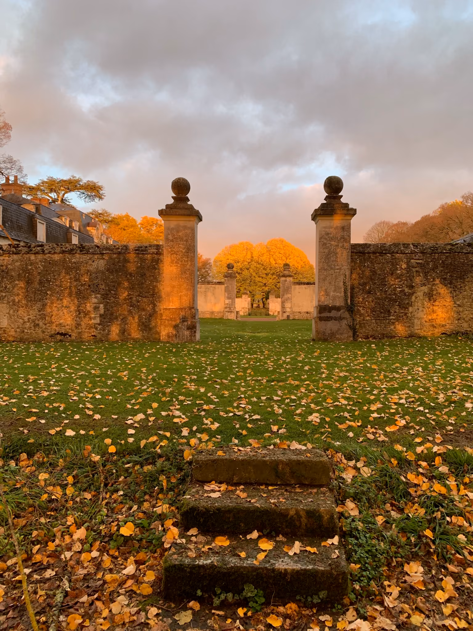 Portail de pierre du parc et pelouse couverte de feuilles d'automne dans la lumière du soir