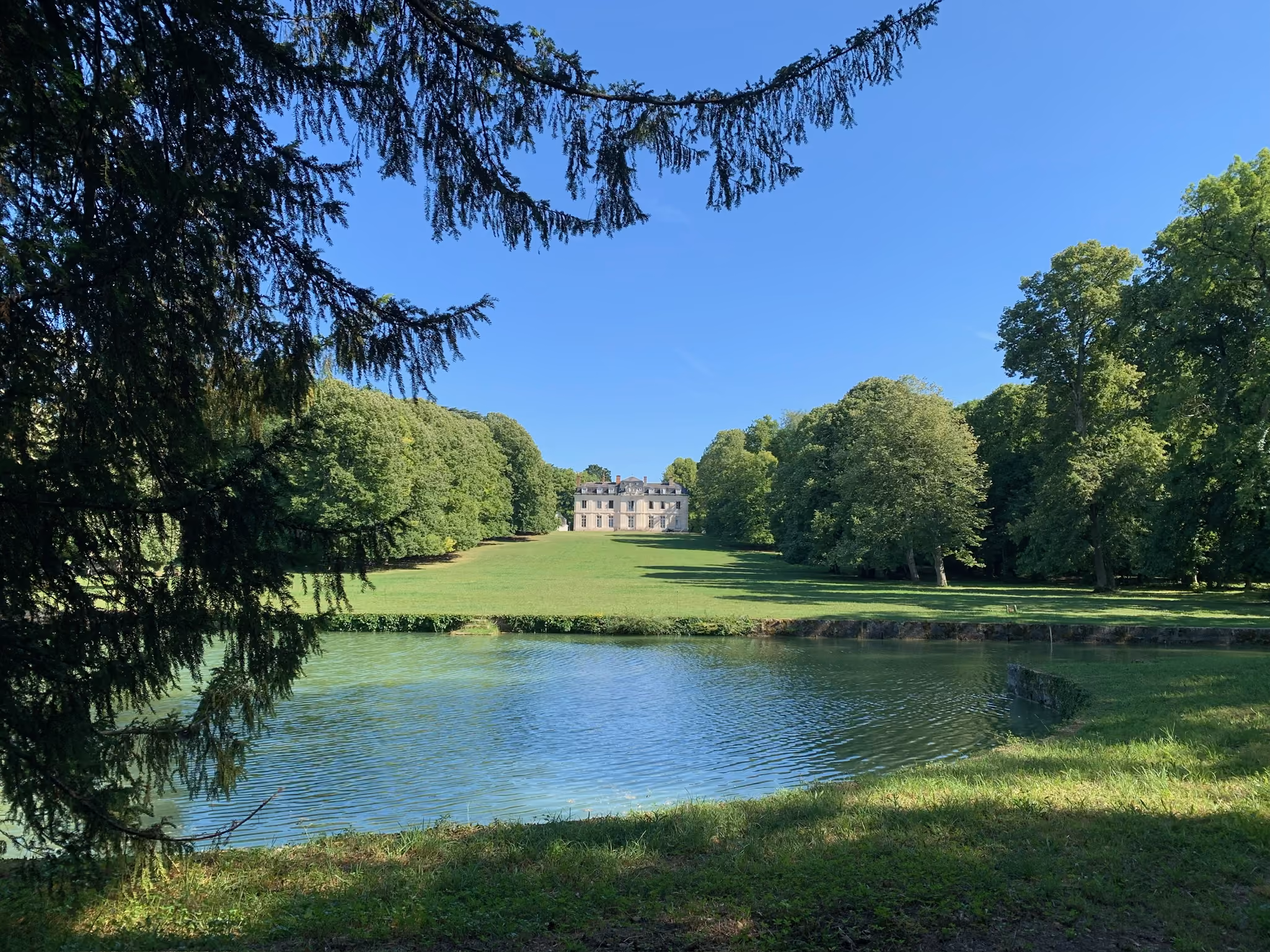 Pièce d'eau et grande perspective de pelouse menant au château un matin d'été