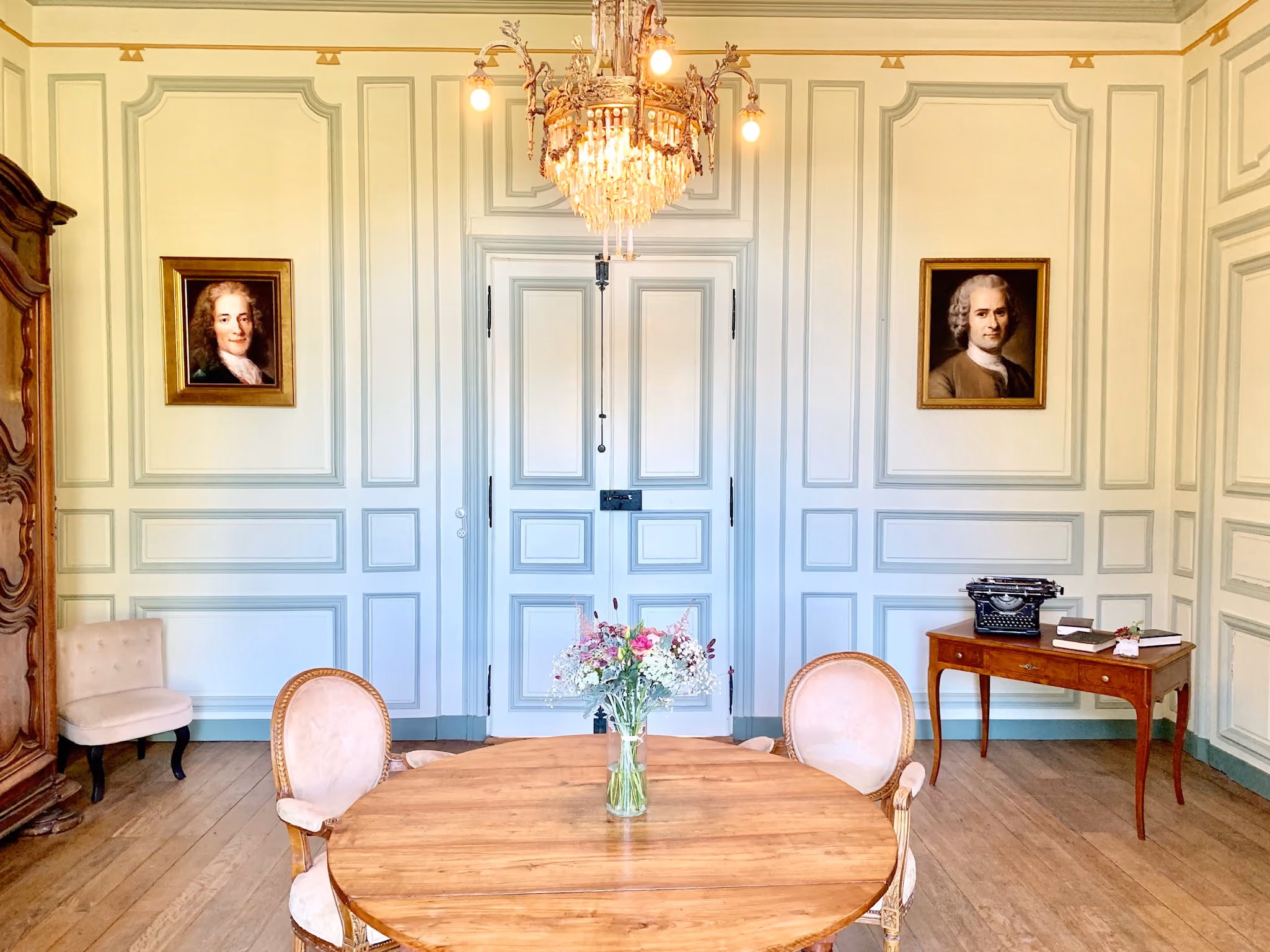 Salon aux boiseries bleu pâle orné des portraits de Voltaire et Rousseau