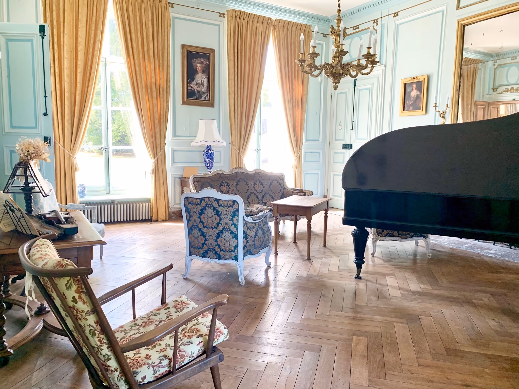 Salon de musique bleu ciel avec piano à queue, lustre doré et parquet ancien