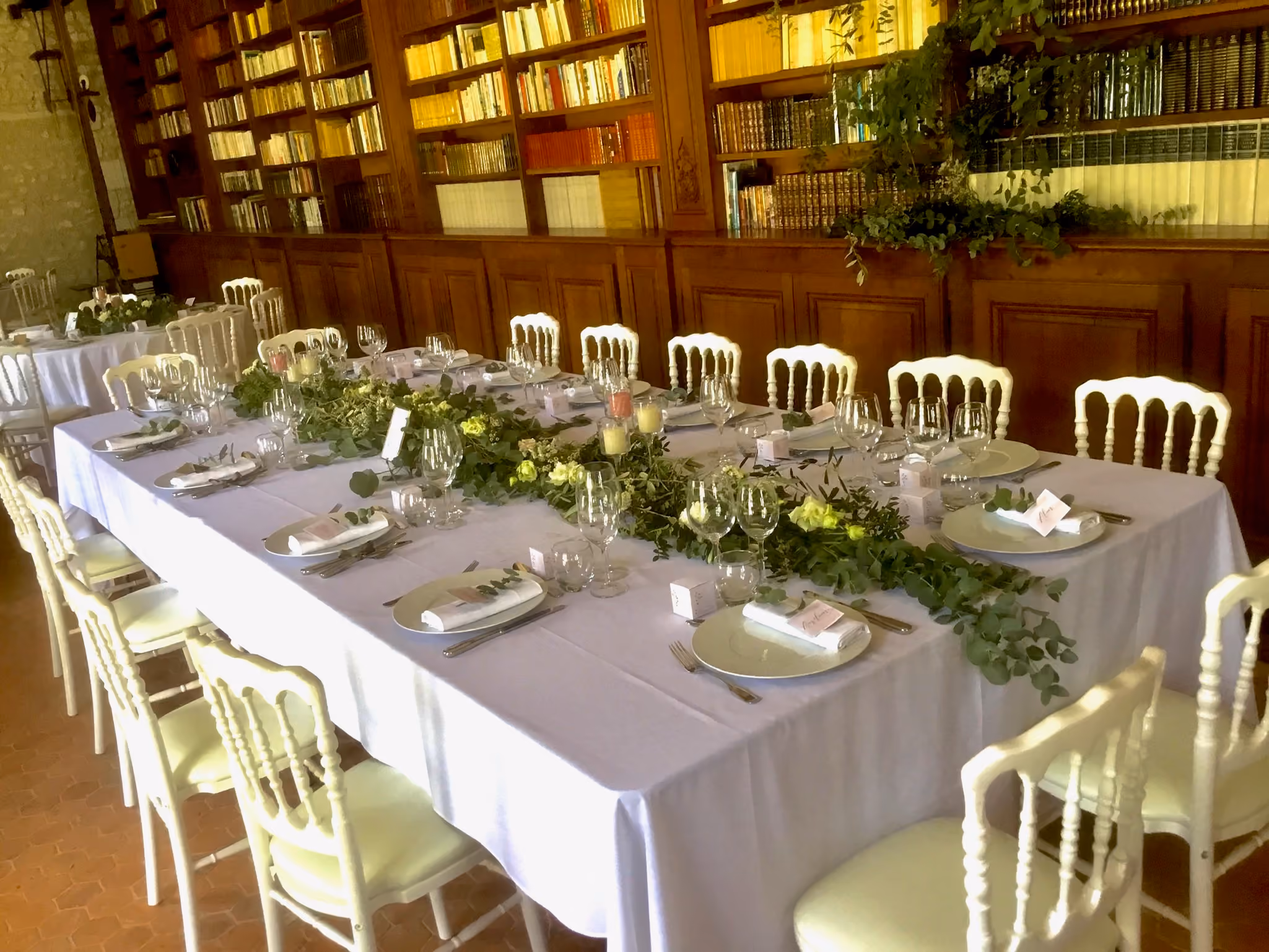 Grande table rectangulaire dressée et suspension végétale devant les rayonnages de la bibliothèque
