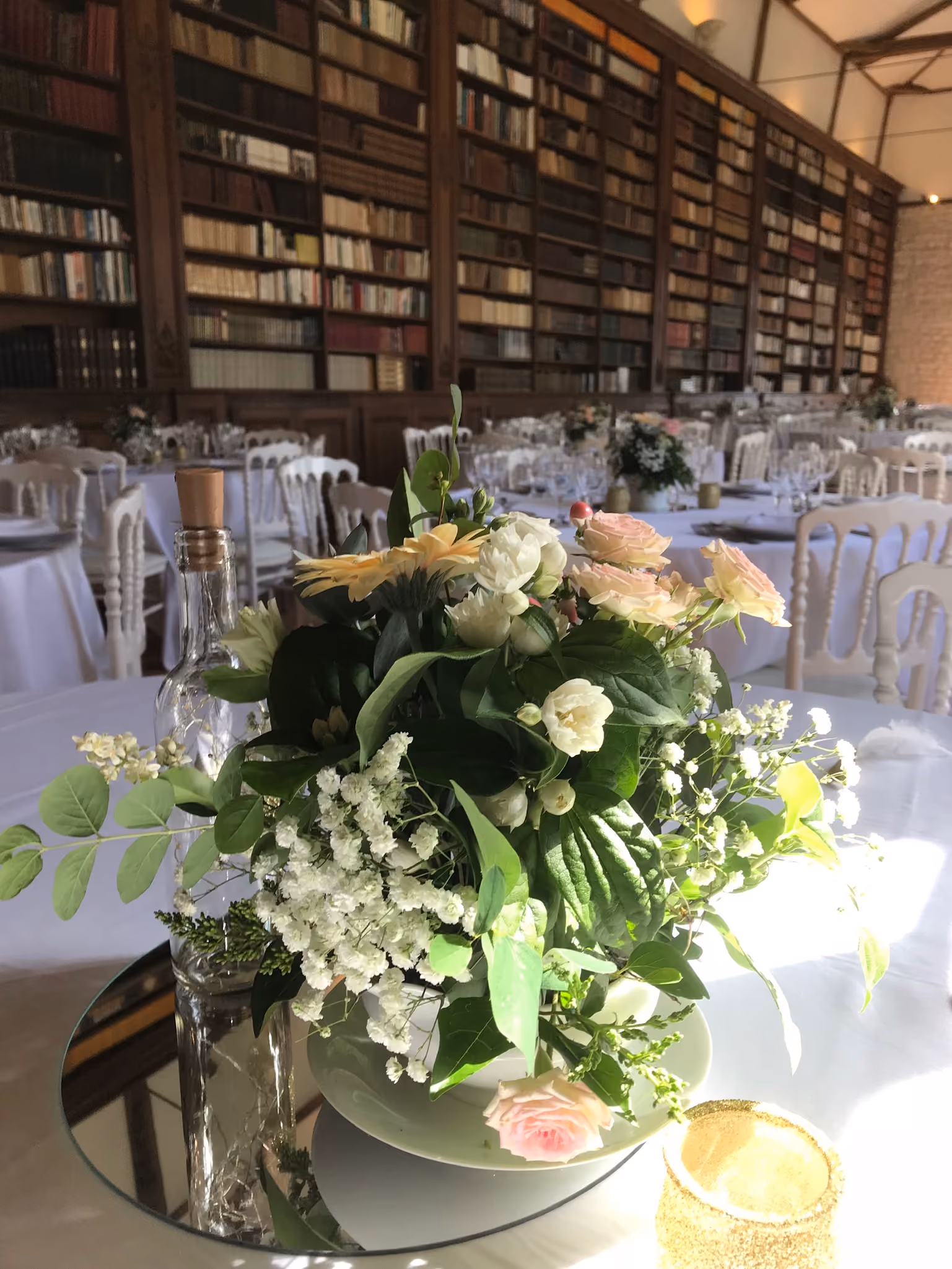 Bouquet de roses pâles sur miroir devant les tables rondes dressées de la salle bibliothèque