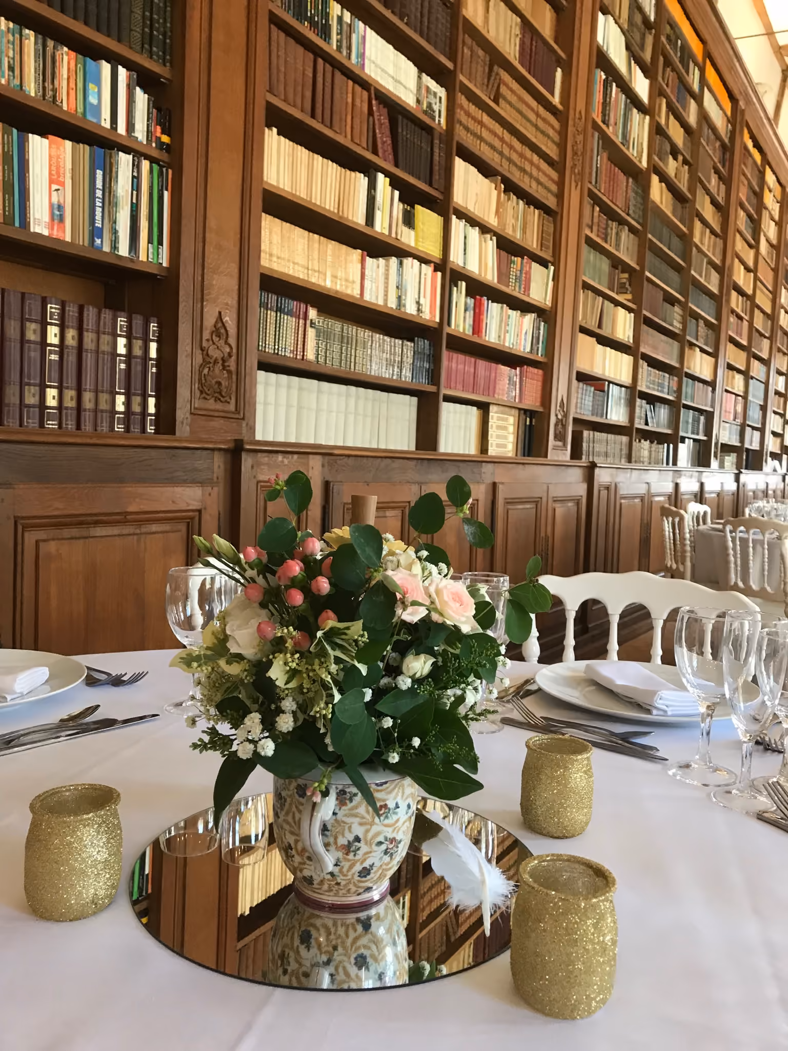 Bouquet en vase de faïence et couverts dressés devant les rayonnages boisés de la bibliothèque
