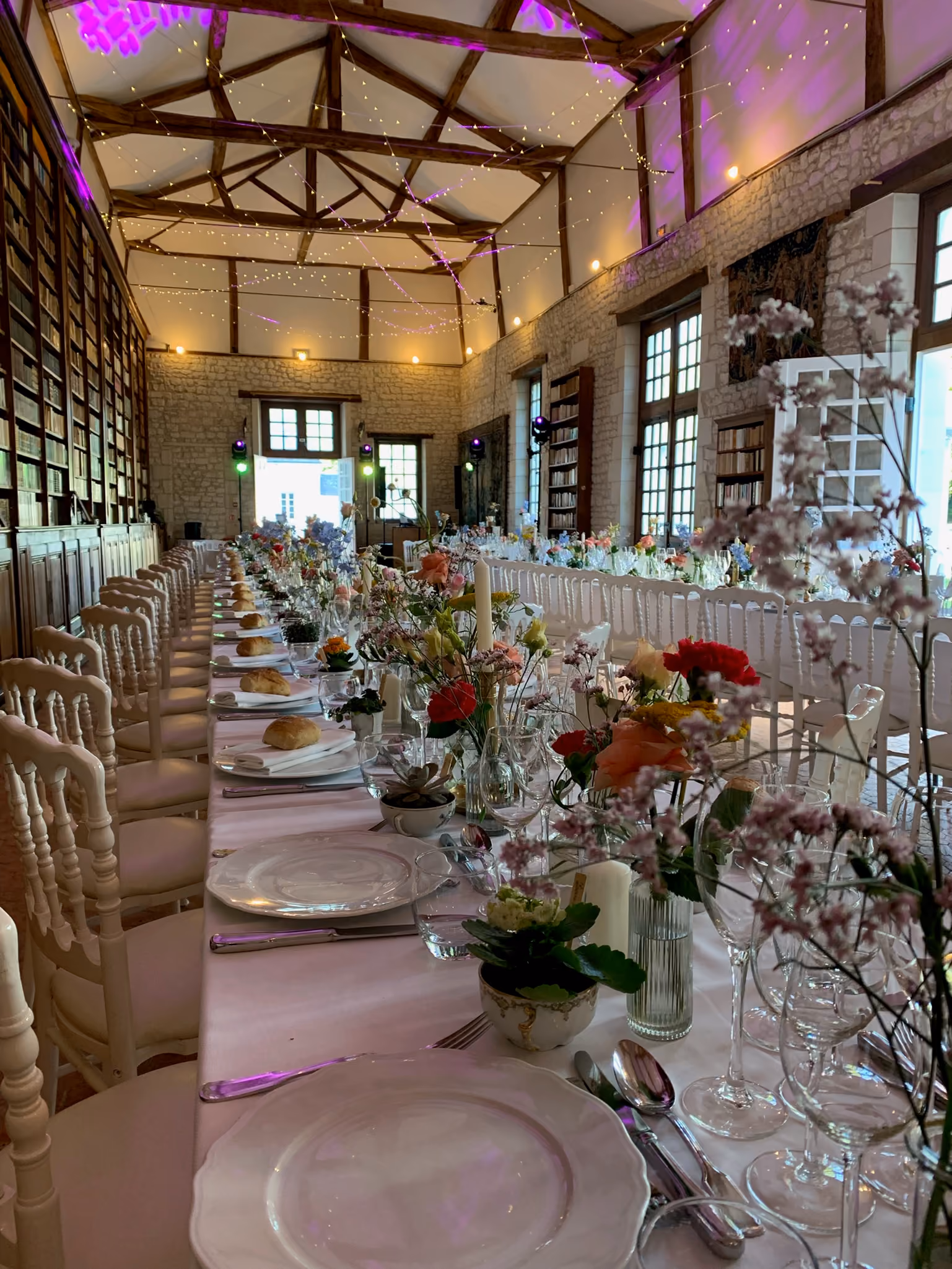 Longue table de banquet fleurie dressée dans la bibliothèque sous des guirlandes lumineuses