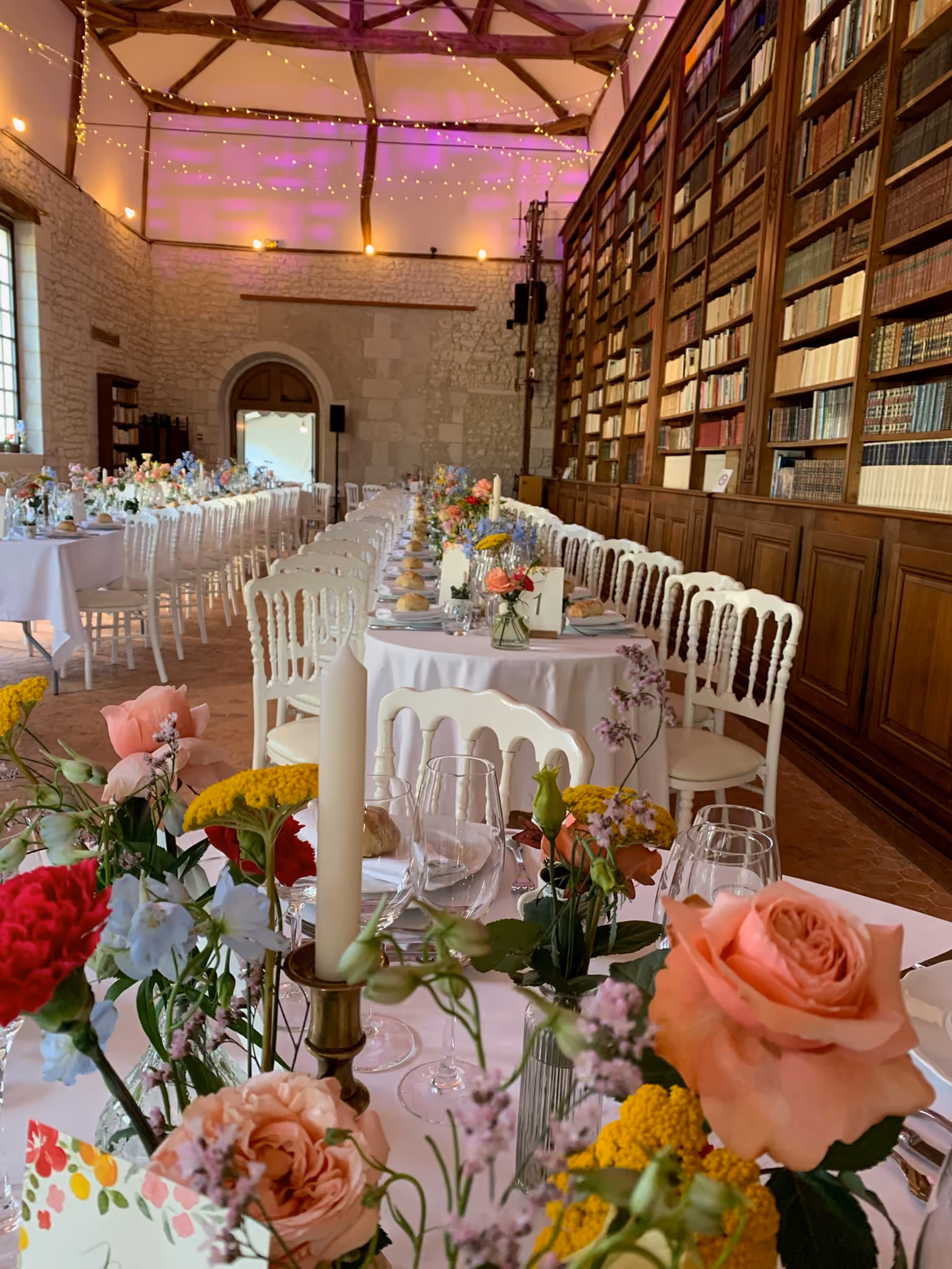 Tables dressées en enfilade et bouquets champêtres devant les rayonnages de la bibliothèque